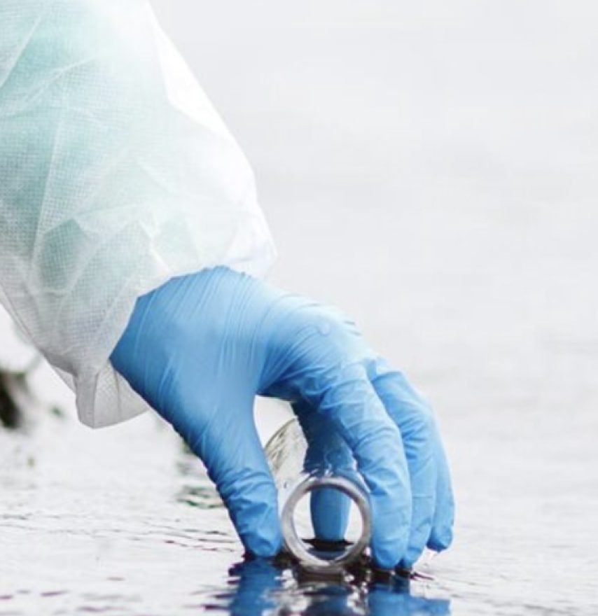 Gloved hand collecting a water sample in a glass vial